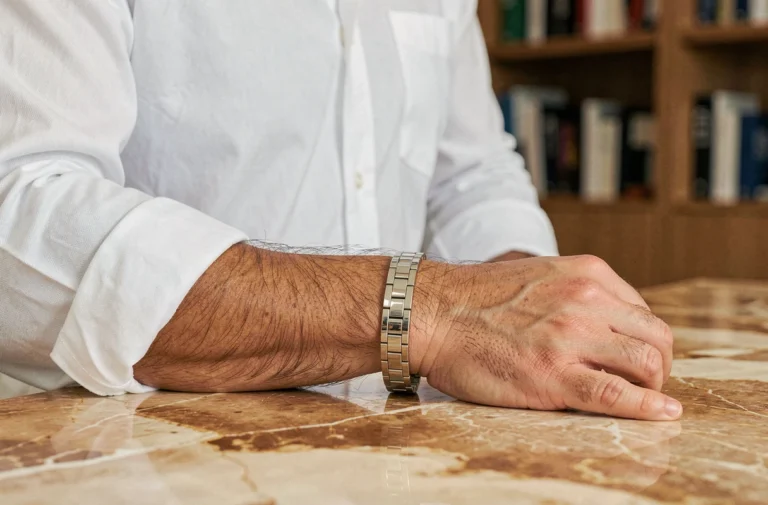 Homme en chemise blanche portant un bracelet en or blanc sur fond de marbre dans un bureau moderne